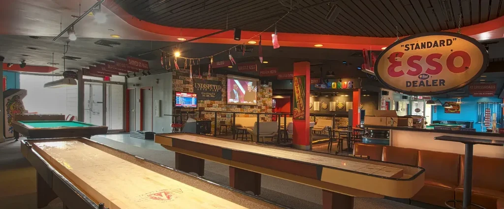 Casual entertainment venue with shuffleboard, pool, arcade, bar, and retro decor.