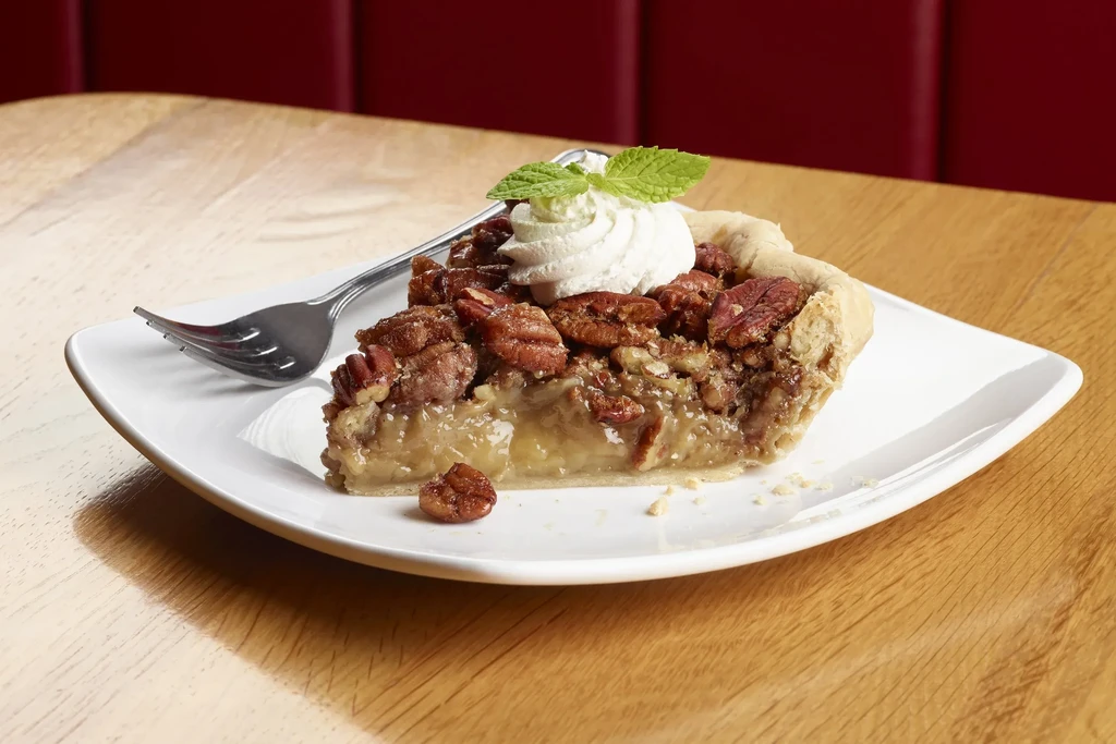 Pecan pie slice with whipped cream, mint leaves, and fork.