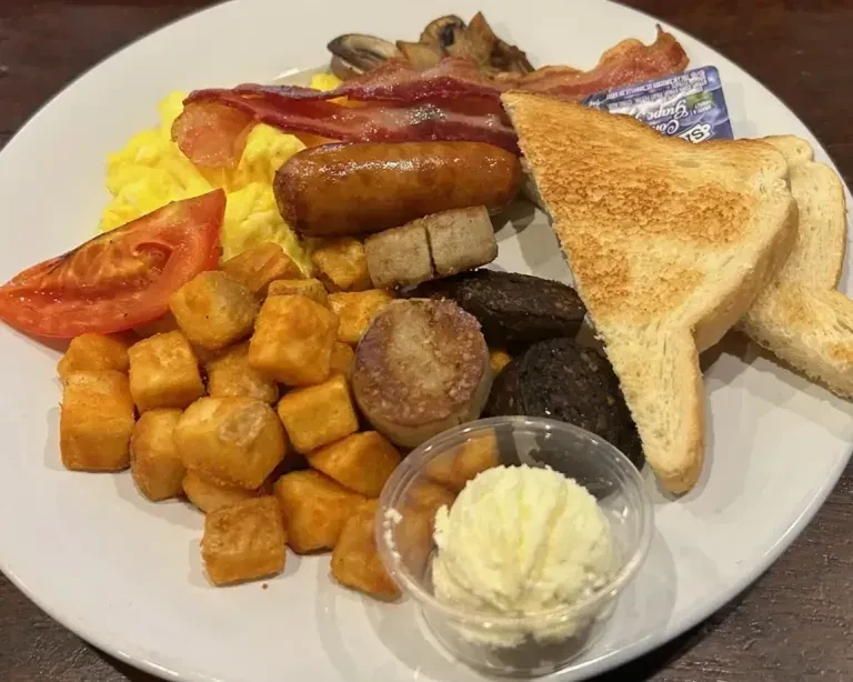 Well-lit full breakfast plate with eggs, bacon, sausage, black pudding, toast.