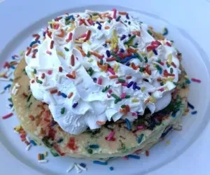 Stack of funfetti pancakes topped with whipped cream and candy sprinkles.