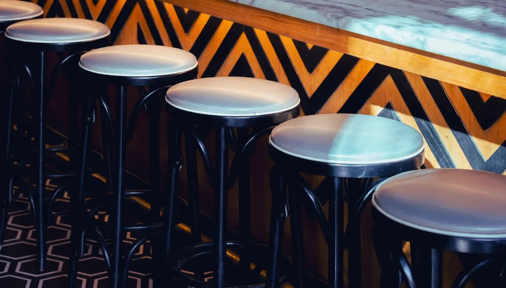 Row of black-framed bar stools with light seats and geometric wall.