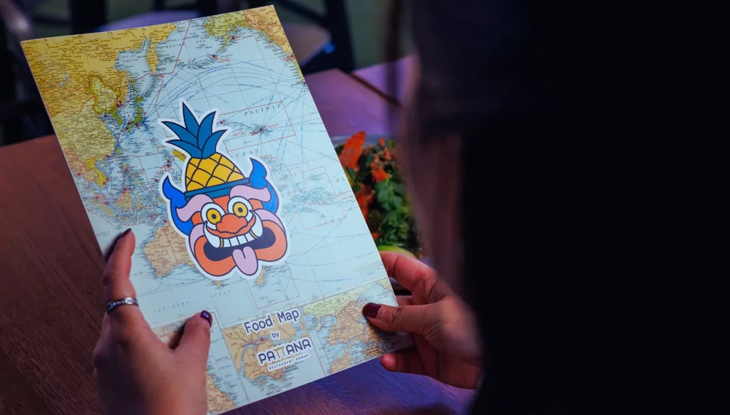Hands hold a world map menu featuring a pineapple logo and restaurant name.