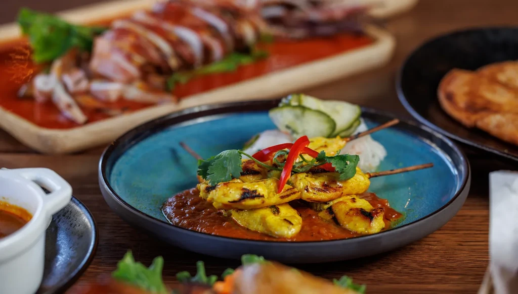Chicken satay skewers with peanut sauce and cilantro in a teal bowl.
