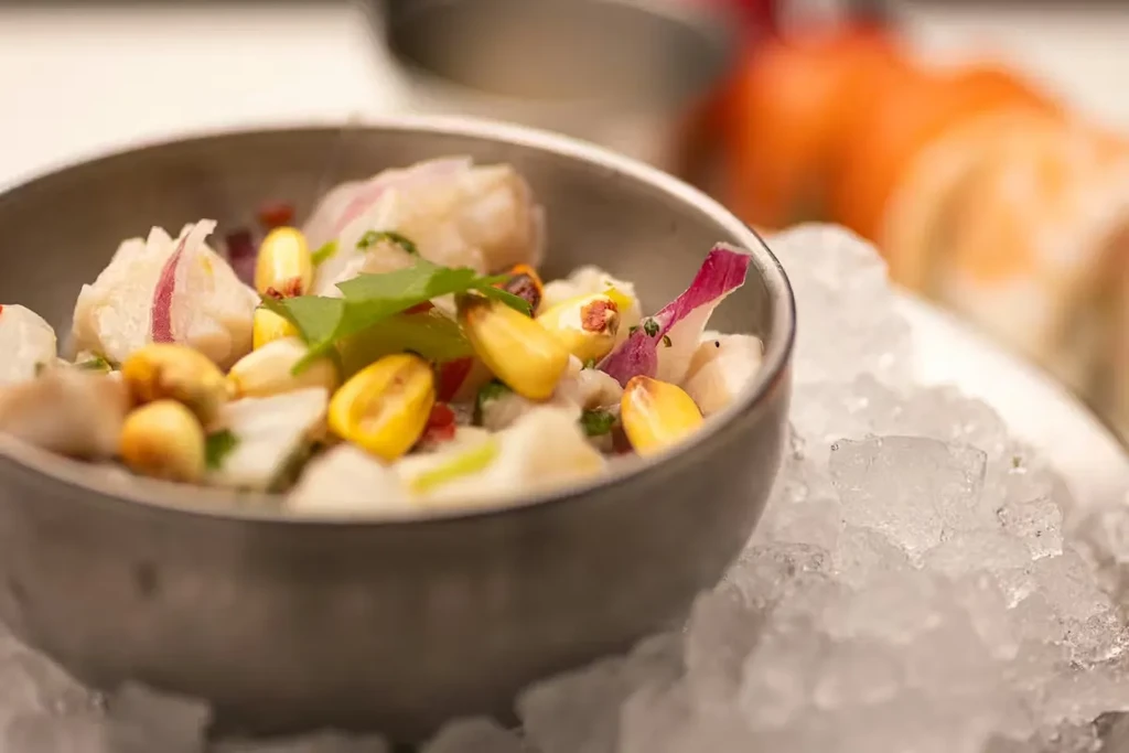 Close-up of ceviche with fish, corn, onion, cilantro on crushed ice.