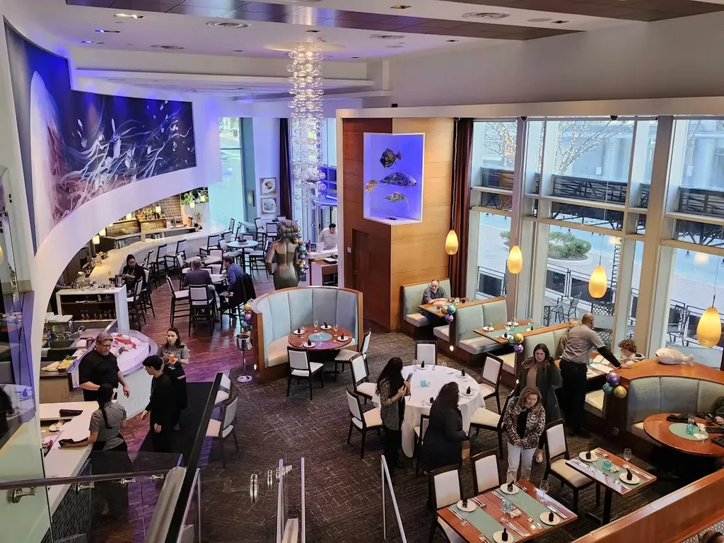 Modern, upscale restaurant interior featuring a bar, chandelier, and window view.