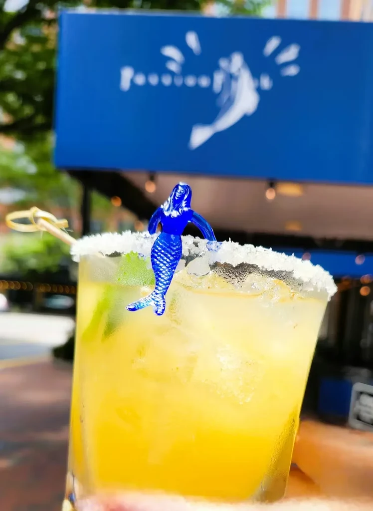 Cold yellow cocktail with salt rim and mermaid garnish, held outdoors.