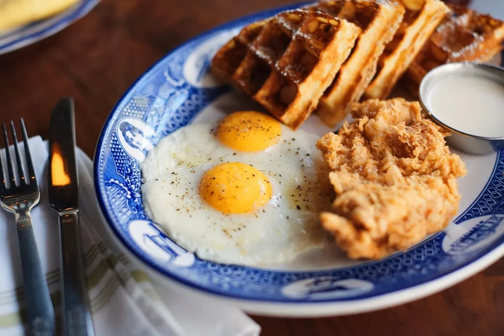 Close-up: blue plate with waffles, sunny-side eggs, fried chicken, ramekin.