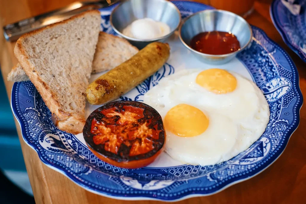 Blue plate with sunny-side eggs, grilled sausage, toast, and tomato.