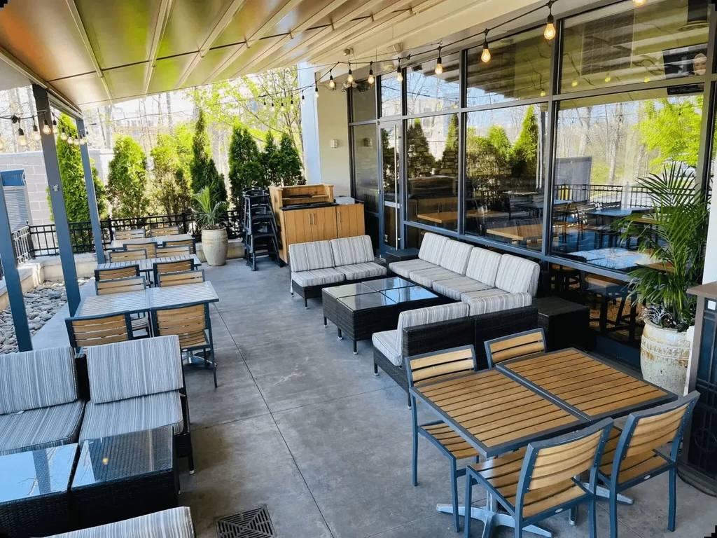 Outdoor restaurant patio featuring mixed seating, awning, string lights, and greenery.