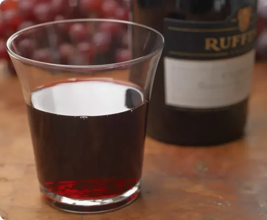 Red wine glass, Ruffino bottle, and grapes on a wooden surface.