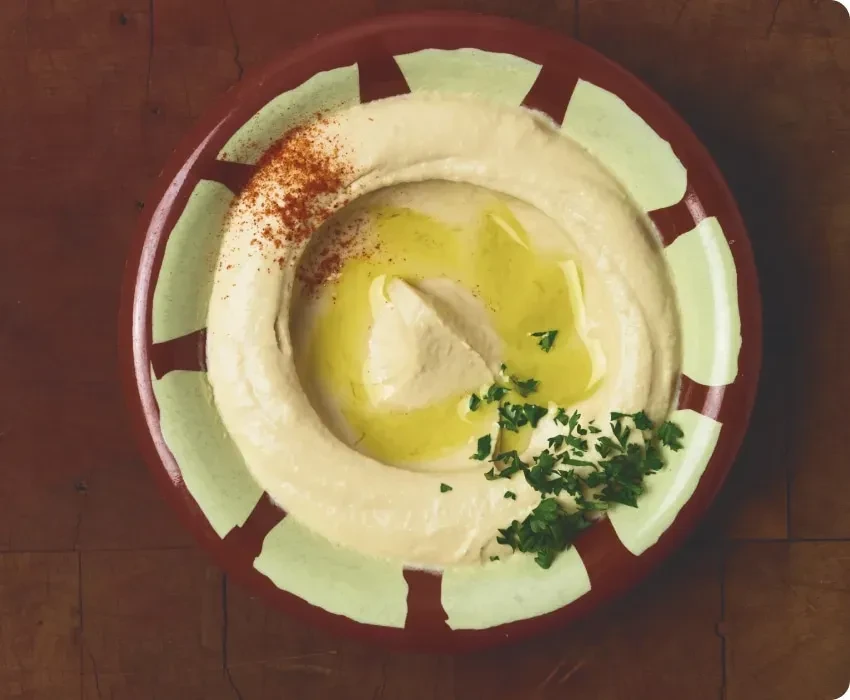 Hummus with olive oil, paprika, and parsley in a rustic bowl.