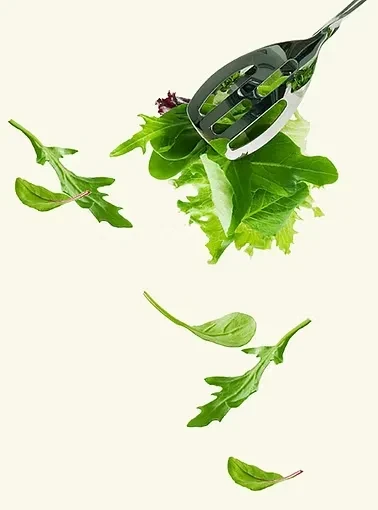 Metallic tongs tossing fresh salad greens against a plain background.