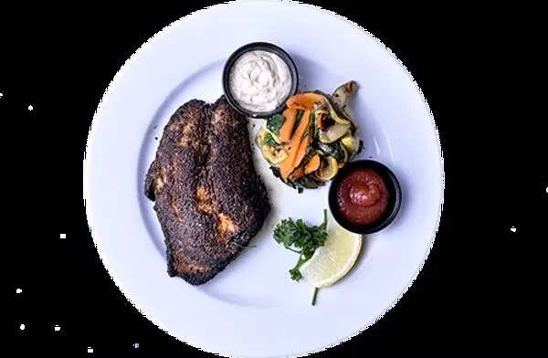 Top-down view of a blackened fish meal with vegetables and sauces.