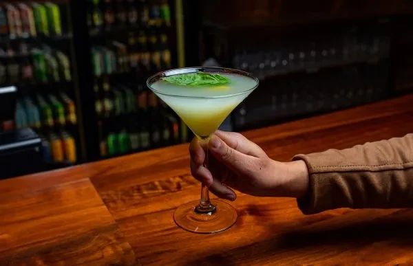 Two-toned cocktail in martini glass, garnished, held at a bar.