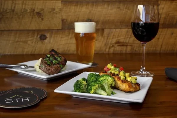 Grilled steak and fish dishes, beer, and red wine on wood.
