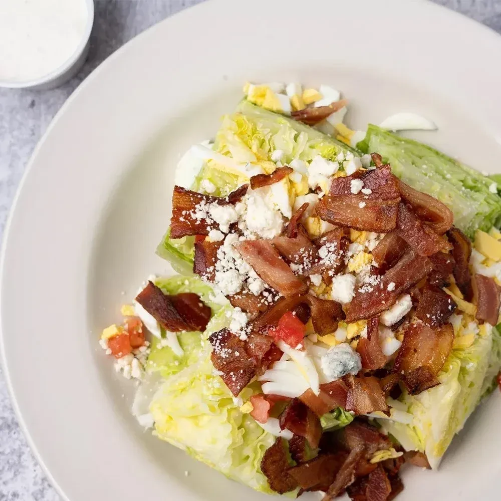 Overhead close-up: wedge salad with bacon, cheese, egg, tomatoes.