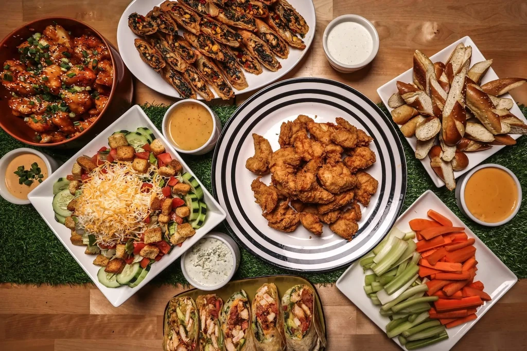 Overhead: Appetizer spread with glazed chicken, spring rolls, salad, pretzels.