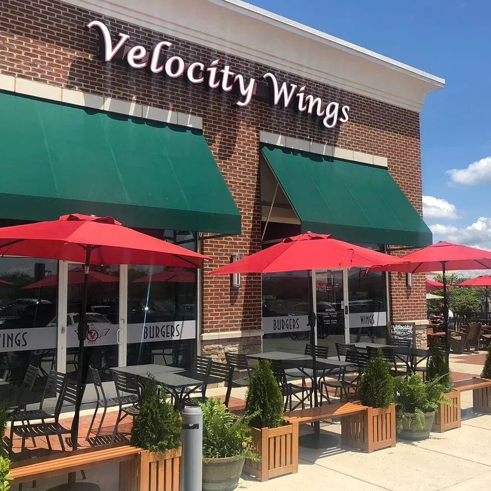Velocity Wings brick restaurant exterior with outdoor dining under red umbrellas.