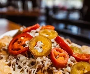 Plate of nachos with melted cheese, ground meat, and assorted pickled peppers.