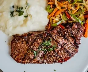 Seared steak, mashed potatoes, and sautéed vegetables on a white plate.