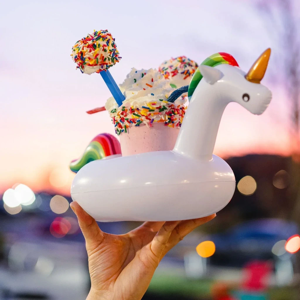 Hand holding a pink milkshake with toppings in a unicorn floatie.