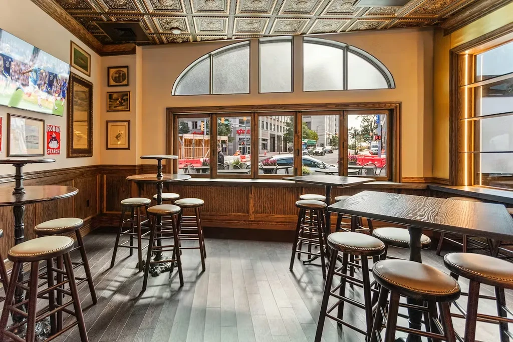 Traditional pub interior with dark wood, pressed-tin ceiling, and sports on TV.
