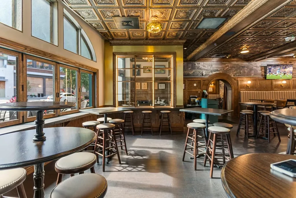 Bar interior with wood paneling, ornate tin ceiling, and sunny windows.