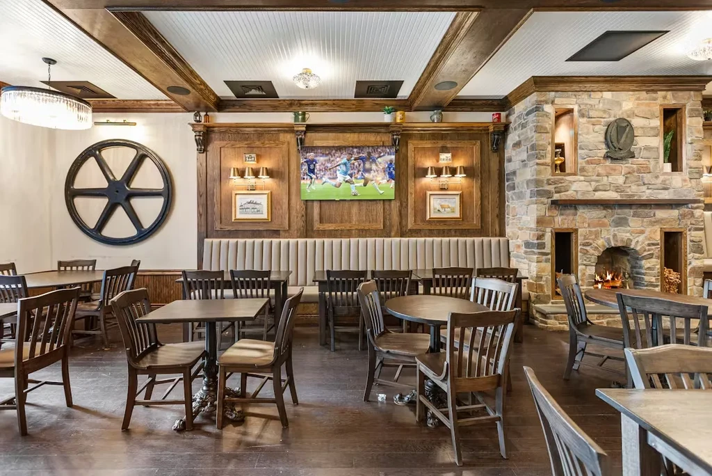 Rustic restaurant with wooden tables, stone fireplace, and sports on TV.