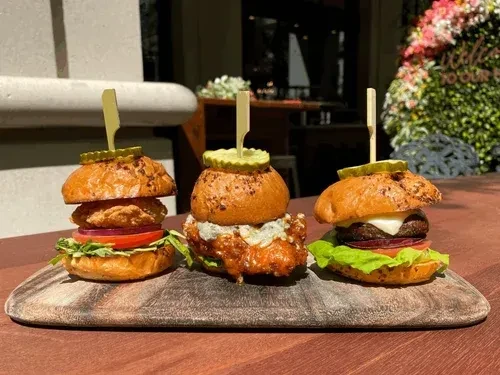 Three varied sliders on a wooden board in an outdoor setting.