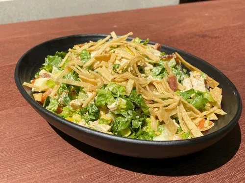 A dark bowl of chicken salad topped with crispy tortilla strips.