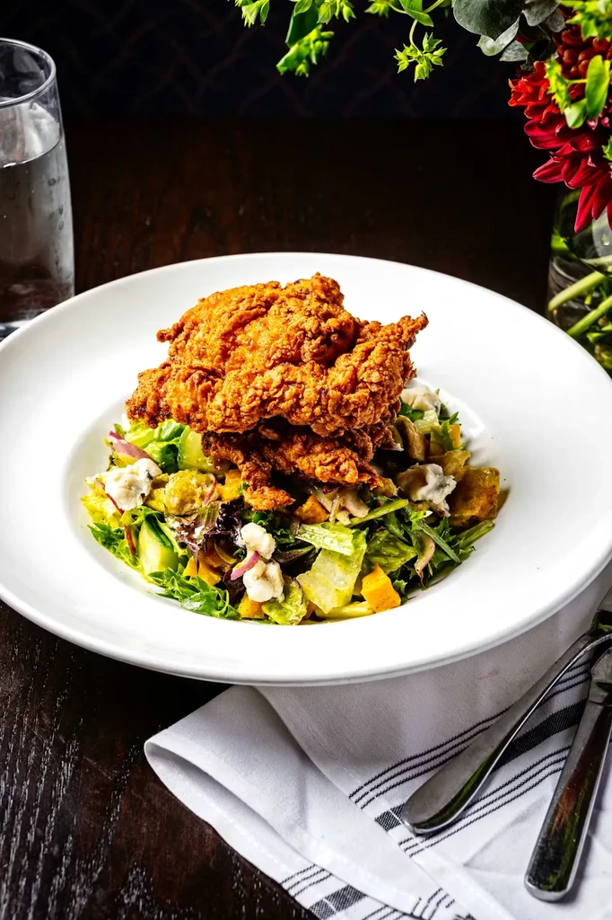 Crispy fried chicken pieces stacked on a colorful mixed green salad.