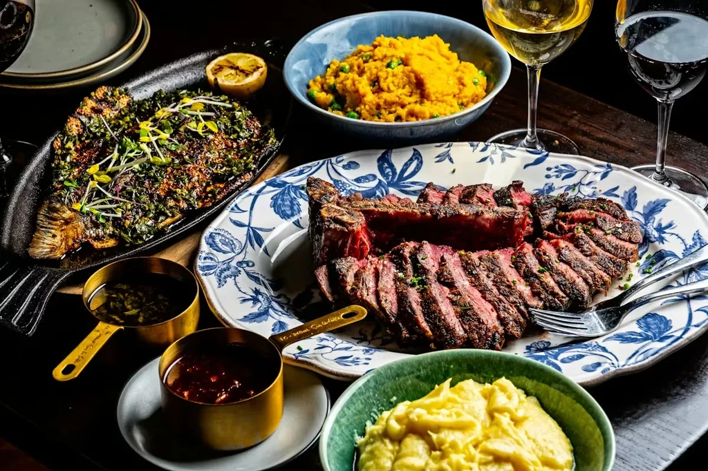 Meticulously plated steak, fish, sides, and wine on a dark table.