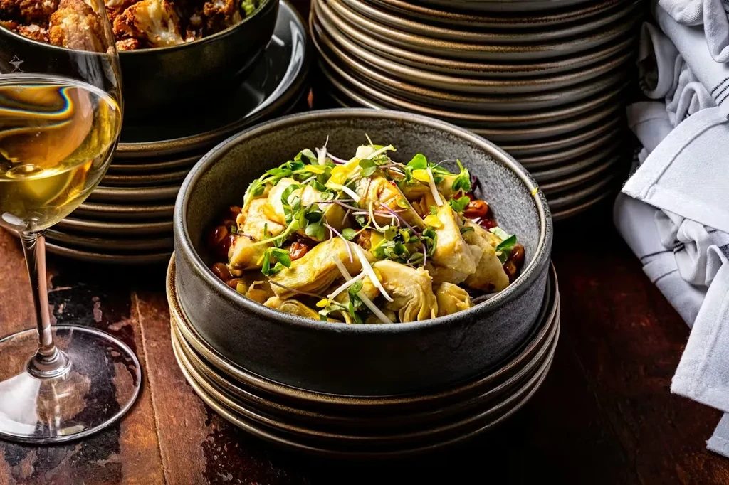 Marinated artichoke hearts, white wine, and roasted vegetables on a dark table.