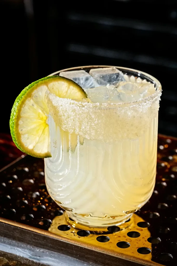 Pale yellow cocktail with lime slice, crushed ice, and heavily rimmed glass.