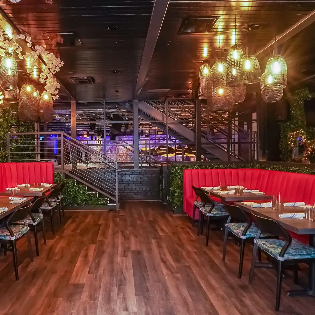 Modern multi-level restaurant interior with red booths, foliage walls, and industrial ceiling.