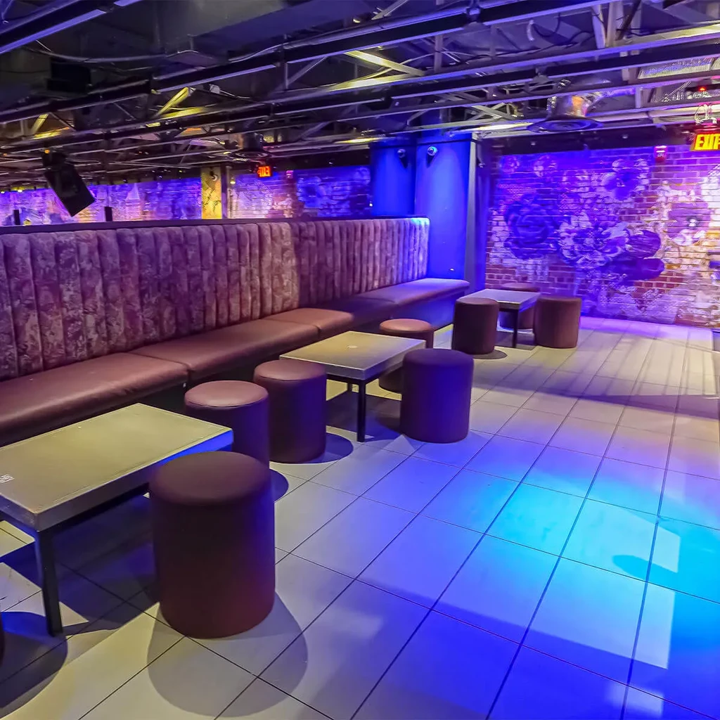 Modern lounge with blue lighting, exposed brick, and velvet seating.