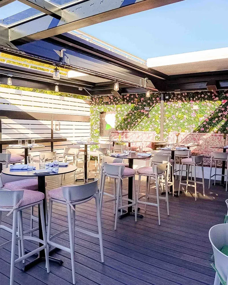 Outdoor patio with pink high-top seating and green floral wall.
