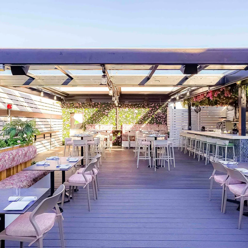 Outdoor rooftop restaurant with pink seating, mint bar, flower wall.
