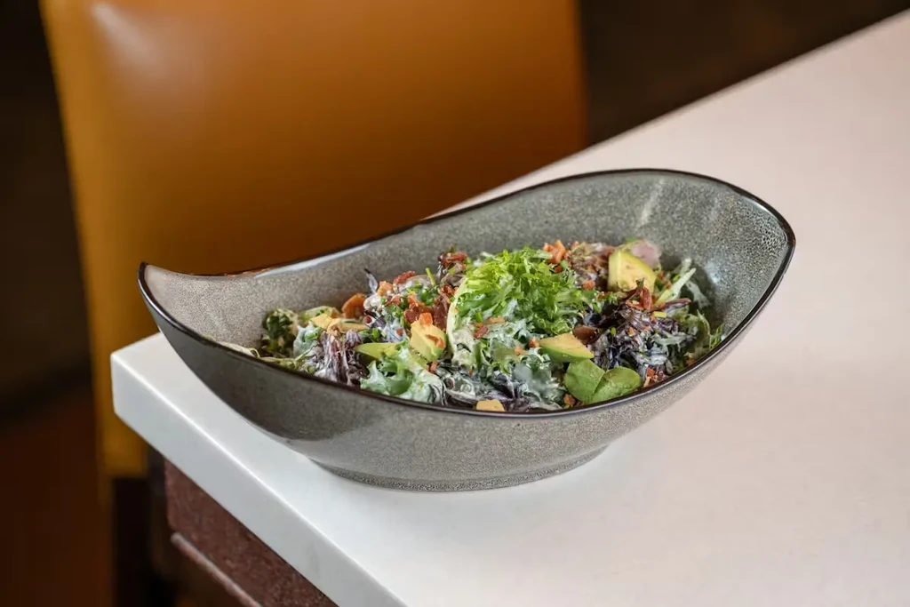 Gourmet salad with avocado, bacon, creamy dressing in a boat-shaped bowl.