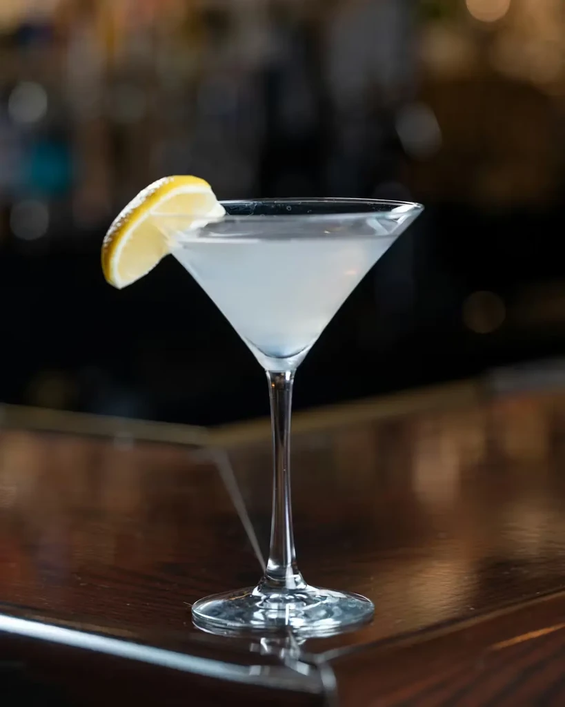 Light cocktail in a martini glass with lemon on a wooden bar.