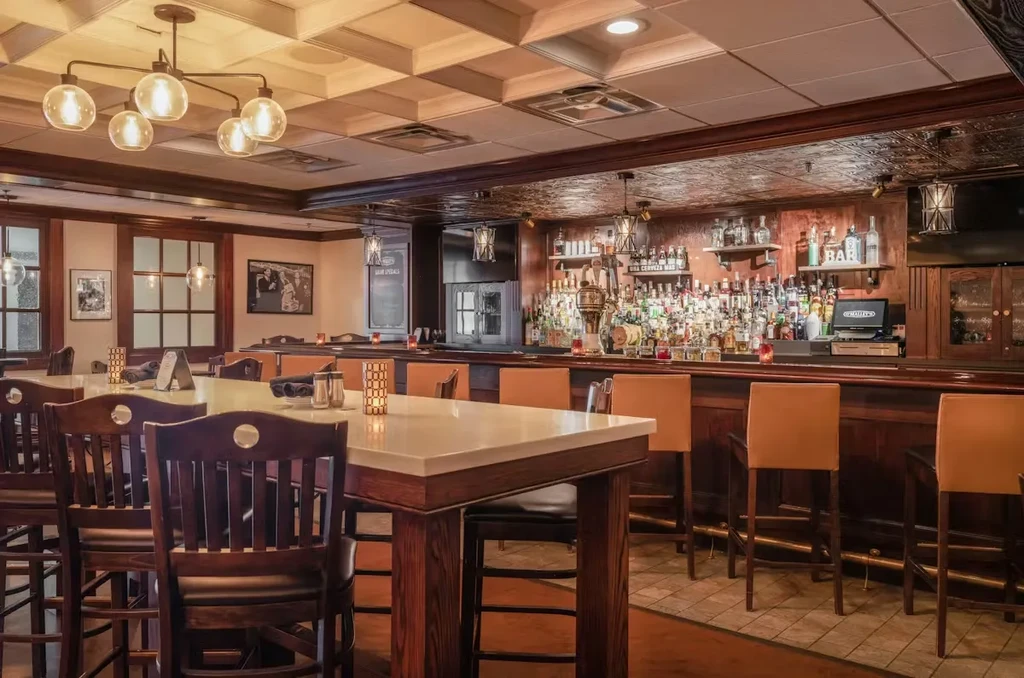 Empty, elegant restaurant and bar with high-top tables and stocked bottles.