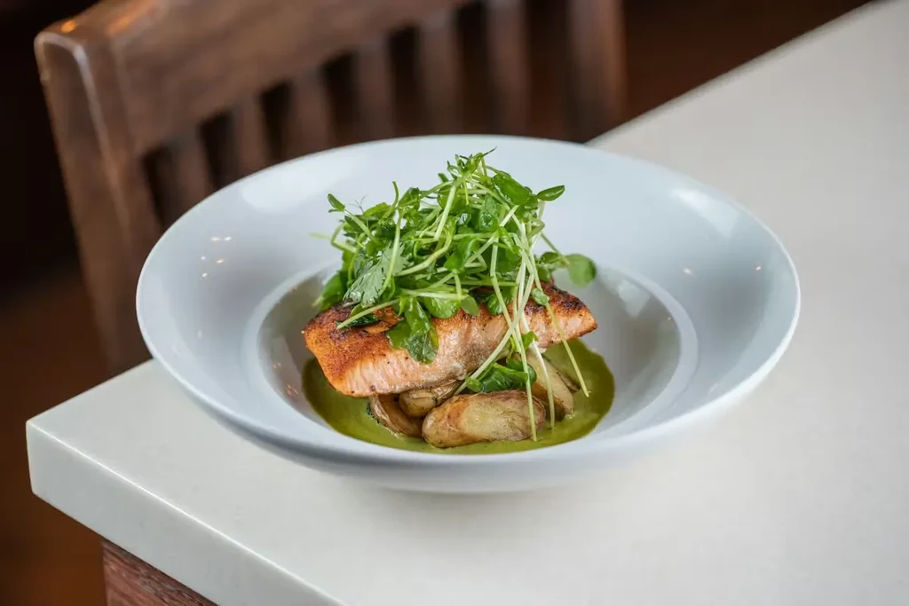 Crispy-skinned salmon, roasted potatoes, vibrant green sauce, and microgreens.
