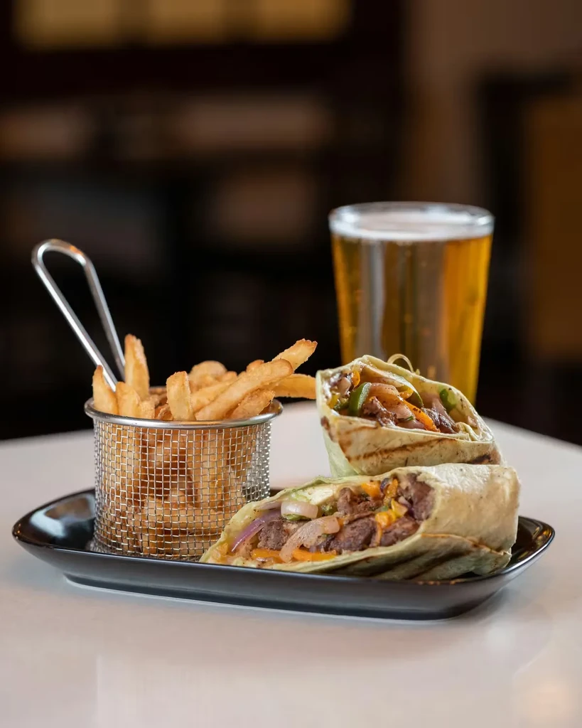 Sliced beef wrap, French fries in basket, and blurred beer.