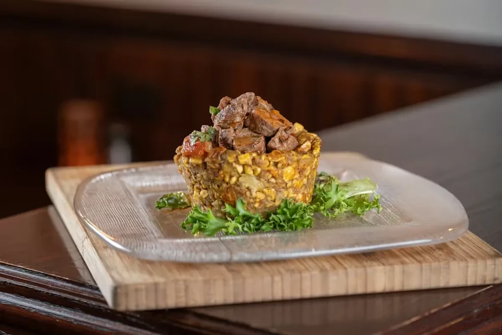Textured mofongo topped with diced meat and herbs, served on a board.