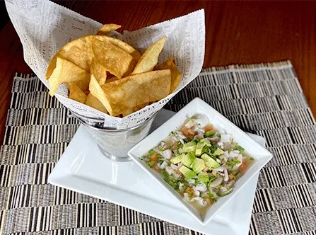 Golden plantain chips and avocado-topped ceviche on a black and white placemat.