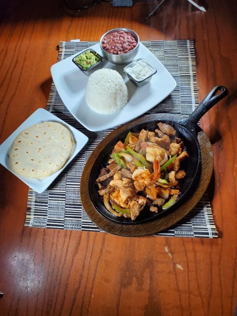 Sizzling mixed fajitas with tortillas, rice, beans, guacamole, and cream.