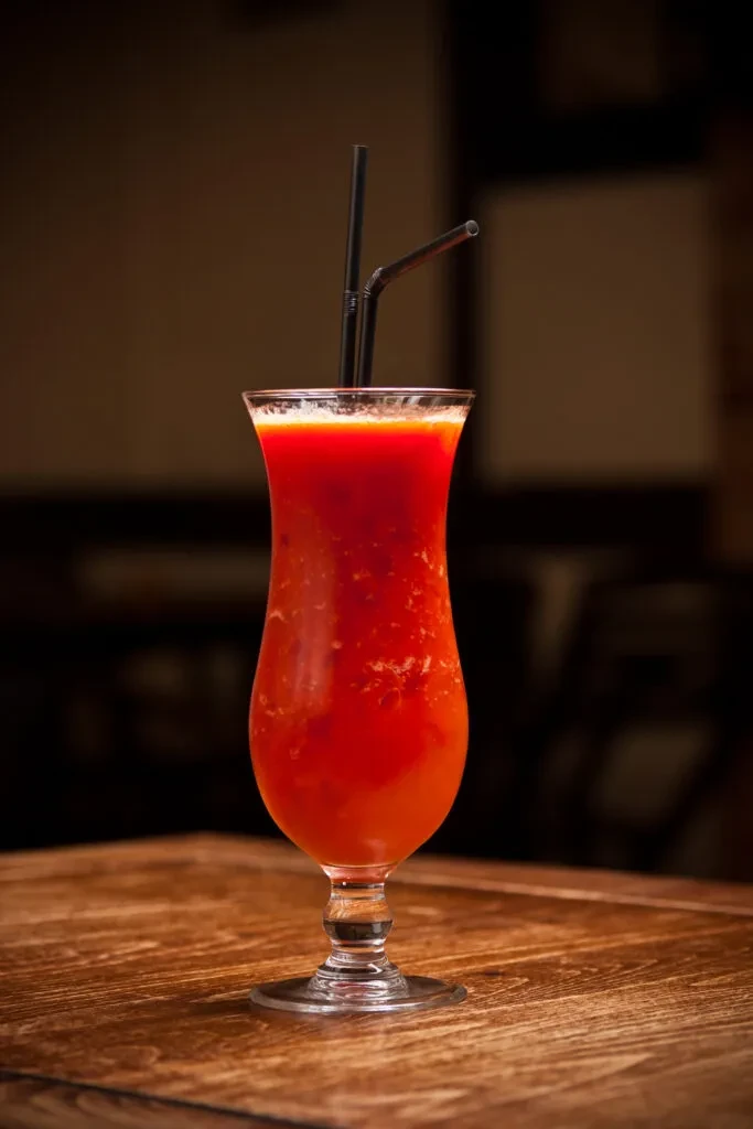 Red frothy blended drink in hurricane glass with two black straws.