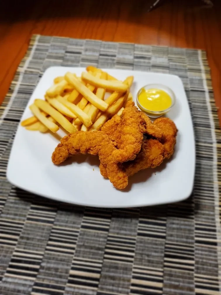 Fried chicken tenders, french fries, and yellow sauce on a white plate.