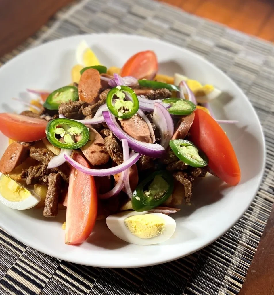 Vibrant plate of meat, sausage, egg, tomato, onion, and jalapeño.
