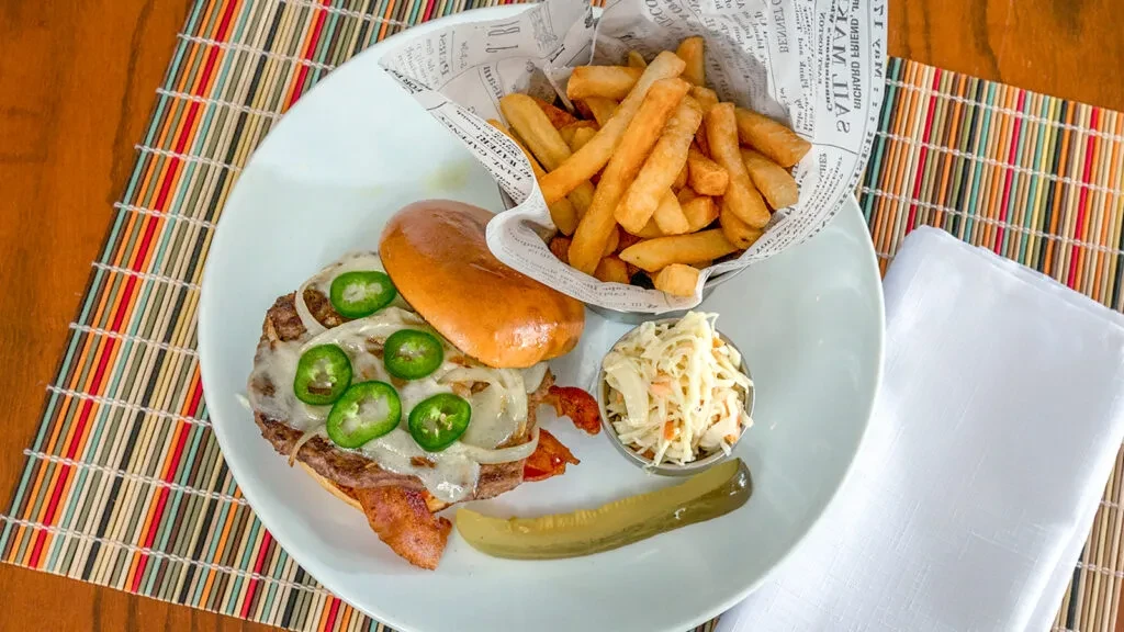 Overhead: open-faced burger, fries, coleslaw, pickle on striped placemat.